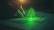 © AhmadTriwahyuutomo - A hand sketches a glowing green tree on paper, symbolizing creativity and growth in a dimly lit setting.