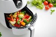© Hafazho - A close-up of an air fryer with a basket full of crispy vegetables, symbolizing healthy eating