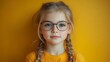 © kenshin - Young girl with blonde hair and pigtails wearing glasses, looking at the camera, against a yellow background.