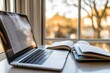 © isti - A laptop and notebooks on a table by a window, creating a study or work environment.