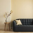 © Sharif54 - A modern black sofa with a wooden side table and a vase with dried flowers in a minimalist living room setting