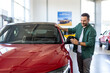 © Graphicroyalty - Handsome man buying new car, standing at car salon and checking automobile. Smiling guy looking at beautiful red auto in showroom