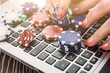 © Svyatoslav Lypynskyy - A woman's hands, adorned with vibrant gambling chips, gracefully navigate a laptop keyboard, embodying the thrill of online casino play during leisurely hours.