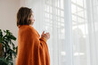 © Westend61 - Thoughtful girl wearing blanket and standing with glass of tea near window at home