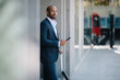 © Westend61 - Businessman standing with smart phone near building at footpath