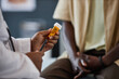 © Seventyfour - Closeup of African American doctor holding plastic bottle with prescription pills while explaining medication and side effects to patient in clinic