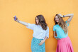 © Iryna - Two young women school girl taking selfies against vibrant orange wall