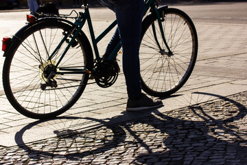 Old classic vintage bicycle wheels, spokes shadow. Bike leave contrasting shadows on asphalt, paved street. A bike rider at sunset on the city street. Travel, sport, ecological transportation concept.