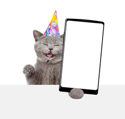 Aufkleber - Happy cat wearing party cap shows big smartphone with blank screen above empty white banner. Empty space for text. isolated on white background
