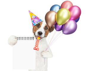 Poster - Happy jack russell terrier puppy wearing party cap holds balloons,  blows in party horn and shows blank list. Empty space for text. isolated on white background