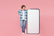 © ViDi Studio - Full body young woman she wears blue shirt white t-shirt casual clothes big huge blank screen mobile cell phone smartphone with area do winner gesture isolated on plain pastel light pink background.