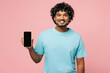 © ViDi Studio - Young Indian man wear blue t-shirt casual clothes hold in hand use mobile cell phone with blank screen workspace area isolated on plain pastel light pink background studio portrait. Lifestyle concept.