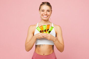 Poster - Young happy woman wear white top casual clothes hold in hand energy protein bars look camera isolated on plain pastel light pink background Proper nutrition healthy fast food unhealthy choice concept