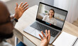 © Prostock-studio - A person gestures while talking during a video call on a laptop, smiling at a cheerful participant. The setting is a cozy home office filled with natural light.
