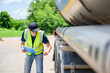 © เลิศลักษณ์ ทิพชัย - A safety inspector inspects the tires of a big fuel tanker while wearing a reflective vest. He maintains adherence to transportation safety regulations while holding a clipboard.
