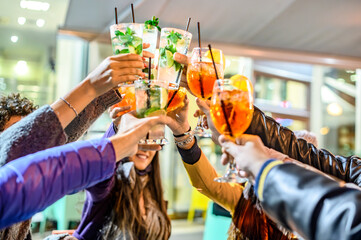 People toasting spritz and mojito drink at fashion cocktail bar restaurant - Young friends having fun together clinking and drinking on happy hour at pub - Friendship, youth and winter party concept