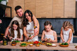 © dvulikaia - Young parents teach their little daughters to cook  at the kitchen.