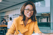 © BullRun - Portrait of positive Japanese female in classic eyewear smiling at camera while spending day for research information and do college course work, happy freelancer working remotely with project