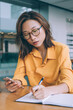 © BullRun - Thoughtful woman writing notes while browsing phone
