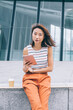 © BullRun - Modern young Asian woman sitting with tablet on parapet