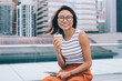 © BullRun - Carefree Asian young woman drinking coffee on urban bench