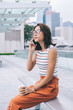 © BullRun - Side view of attractive Chinese female tourist with coffee to go taking rest at urban setting receiving mobile call for talking and communicating, concept of modern technology and generation z