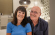 © luciano - Happy relaxed senior couple sitting on bed looking at camera. Smiling elderly man and woman enjoying cuddle moments
