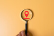 © BritCats Studio - people hand holding magnifier to zoom in the red location mark on color background with copy space. Location sign relating to customer location identification. Location privacy setting online