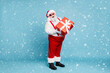 © deagreez - Full length photo of funny funky fat santa claus with big belly abdomen hold gift box for christmas time follow noel tradition wear red pants white gloves boots isolated over blue color background