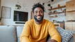© primopiano - Smiling man with dark hair and beard sitting on a couch in a modern living room with yellow sweater and patterned pillow