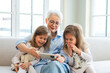 © Юлия Завалишина - Happy family at home. Two little girls sisters twins grandmother enjoying time together watching video on phone. Good time at home. Grandma granddaughters child kids together. Family generations