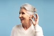 © Maria Vitkovska - Portrait of deaf senior gray haired woman having hearing aid in ear, isolated on blue background