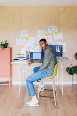 Young web designer sitting at desk working on laptop