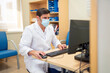 © Santi Nuñez/Stocksy - Doctor working on computer in hospital office with mask