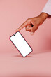 © BONNINSTUDIO/Stocksy - Person pointing at smartphone with blank screen on pink background