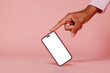 © BONNINSTUDIO/Stocksy - Person pointing at smartphone with blank screen on pink background
