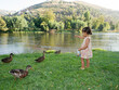 © mahalo studio/Stocksy - Little girl feeding ducks by the river in summer