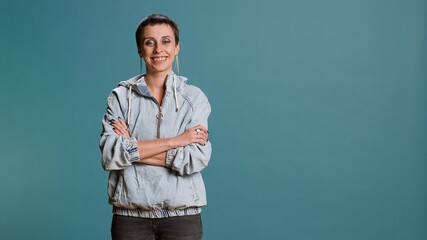 Wall Mural - Portrait of young adult posing with confidence in studio and showing a candid smile, standing with arms crossed and feeling independent. Woman with a groovy cool outfit being cheerful. Camera B.