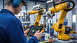 © Hound - A man is holding a tablet in front of two robots. The robots are yellow and are in a factory setting. The man is likely a technician or engineer
