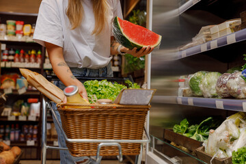 A shopper excitedly picks fresh produce, including a large, juicy watermelon, in a colorful grocery store