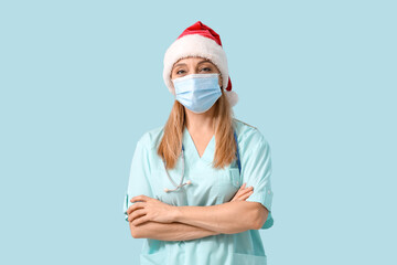 Wall Mural - Mature female doctor in Santa hat and medical mask on blue background