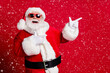 © deagreez - Photo of retired old man grey beard open mouth smile direct fingers empty space demonstrate best option wear santa x-mas costume gloves coat sunglass headwear isolated red color background
