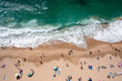 © Andrii - Overhead drone shot of anonymous tourist and colorful parasols on sandy seashore. From above of people enjoying summer vacations at beach during sunny day
