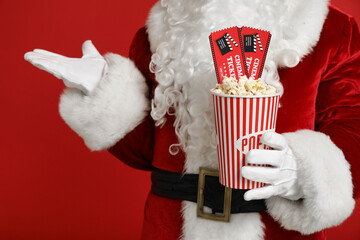 Wall Mural - Santa Claus with bucket of popcorn and cinema tickets on red background. Closeup