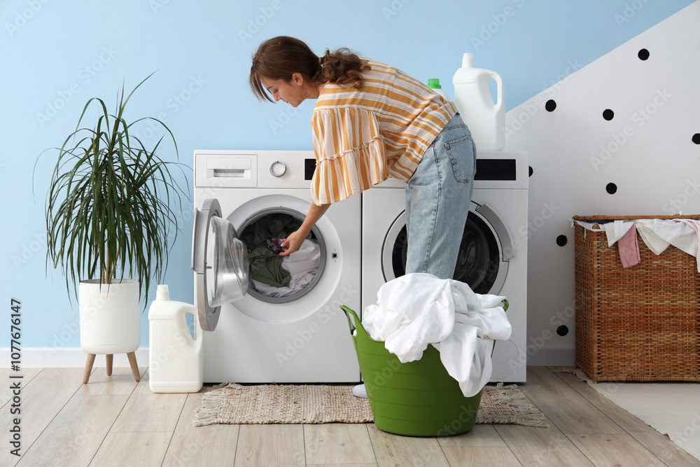Young woman putting laundry detergent into washing machine in room