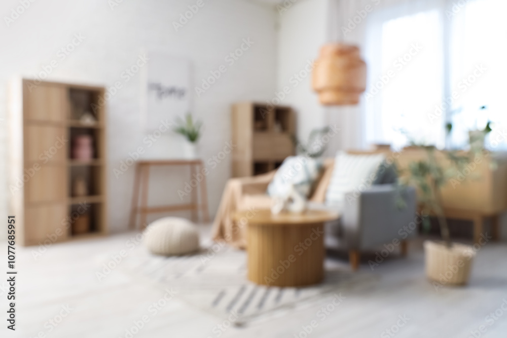 Blurred view of light living room with grey sofa, table and shelf units