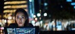 © chic designs - 夜の街の明かりを背景に、ノートパソコンでデータを分析する集中力のある女性