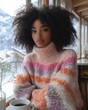 © Digital Artist - Black Woman Wearing a Pink and Purple Striped Oversize Turtleneck Sweater Sitting in a Coffee Shop with a Beautiful View of Nature and Winter Mountain Range