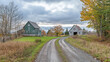 © Sadia - Rustic dirt road leading to two vintage barns amidst autumn foliage and cloudy skies