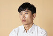 © RHL Studio - Close-up portrait of a asian young man wearing a white shirt, looking thoughtful against a beige background. His expression conveys contemplation and focus, creating a serene and calm mood.